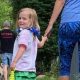 young child walking away from the camera hand in hand with a teacher. Child is looking back at the camera, smiling